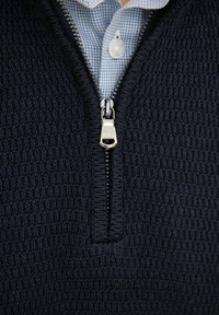 Granatowy sweter na zamek błyskawiczny z fakturowanym wzorem dzianiny, z srebrnym zamkiem i kołnierzykiem jasnoniebieskiej koszuli w kratę pod spodem.