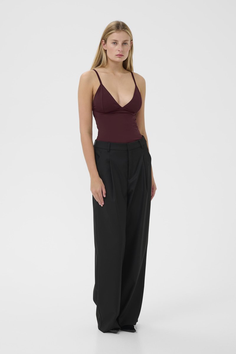 Bordeaux mouwloze bodysuit met een diepe V-hals, gecombineerd met hoge zwarte wijde broek, met een gladde textuur en minimaal ontwerp.