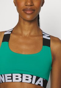 Sujetador deportivo verde con anchas tirantes negras con marca blanca, escote redondeado y una textura suave y elástica.