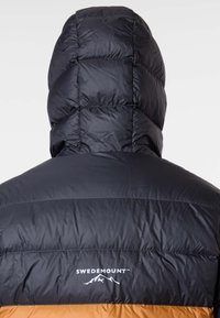 Svart puffjacka med en brun nederdel, med huva, quiltad textur och en vit logotyp på ryggen. Vattentätt material.