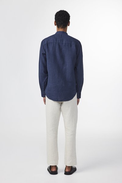 Marineblauwe linnen blouse met lange mouwen en een gebogen zoom, gecombineerd met lichtbeige linnen broeken en zwarte instapschoenen.