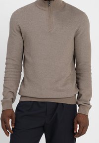 Beige Strickpullover mit hohem Kragen und Viertelreißverschluss. Verfügt über ein strukturiertes Muster sowie gerippte Bündchen und Saum. Einfaches Logo-Detail sichtbar.