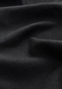 Nahaufnahme eines glatten schwarzen Strickstoffs mit weichen Falten und sichtbaren feinen Texturdetails bei subtiler Beleuchtung.