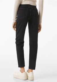 Jeans negros de corte slim, con dos bolsillos traseros y detalles de costura sutiles, combinados con zapatillas blancas para crear contraste.