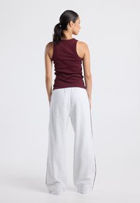 Maroon sleeveless tank top paired with gray wide-leg sweatpants featuring a contrasting side stripe. Soft, lightweight fabric.