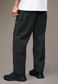 Schwarze Cargo-Hosen aus strukturiertem Stoff, mit Seitentaschen und einer lässigen Passform. Ergänzt durch schwarze Sportschuhe.