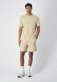 Beige katoenen t-shirt met een reliëf "Champion" logo, gecombineerd met bijpassende shorts. De outfit heeft een ontspannen pasvorm en een eenvoudig ontwerp.