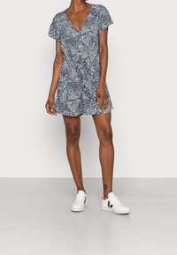Navy patterned short dress with a deep V-neck, short sleeves, and a button front. Paired with white sneakers featuring navy and red accents.