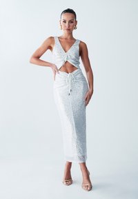 Silver sequin dress with a V-neck, cut-out midsection, and adjustable drawstrings. Floor-length, fitted silhouette with smooth texture.