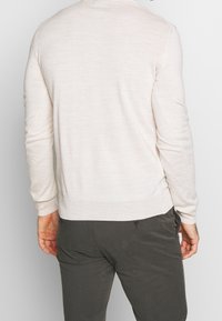 Hellbeige gestrickter Pullover mit Rundhalsausschnitt und langen Ärmeln, kombiniert mit dunkelgrauen Hosen. Weiche Textur, minimalistisches Design und schlichte Ausführung.