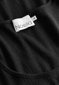 Melna ribota auduma ar gludu tekstūru, ar apaļu apkakli un baltu etiķeti, uz kuras ir uzrakstīts "Noella" un izmērs "S."