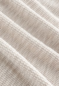 Gestrickter Stoff mit einem beigen und cremefarbenen Farbton, der ein strukturiertes, gewebtes Muster und subtile Unterschiede in der Fadendicke aufweist.