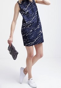 Námořnická bezramínková mini šaty s bílým mramorovým vzorem, s kapsičkou na prsou, v kombinaci se šedým psaníčkem a bílými teniskami. Hladká textilie.