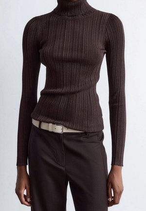 Personne portant un pull à col roulé côtelé marron foncé ajusté, rentré dans un pantalon sombre assorti avec une ceinture blanche.
