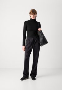 Un col roulé noir, un pantalon de jogging noir ample avec des rayures blanches sur les côtés, et un grand sac à épaule noir. Texture de tissu lisse et design décontracté.