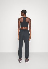 Svart crop top med racerback-design og tettsittende midje, kombinert med svarte joggebukser med elastisk linning og mansjetter, brukt med grå joggesko.