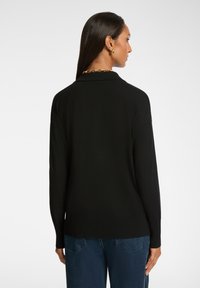 Maglione nero a maglia con taglio rilassato, dotato di orlo e polsini a costine. Texture liscia, senza pattern visibili o dettagli metallici.
