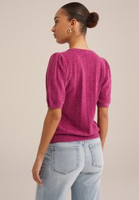 Maglione fucsia lavorato a maglia con maniche a sbuffo corte, motivo a zigzag testurizzato e orlo a coste, abbinato a jeans azzurri a vita alta.