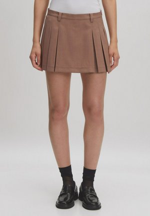 Bruine geplooide rok met een aansluitende taille, gemaakt van textuurstof, gecombineerd met zwarte loafers en gestreepte zwarte sokken.