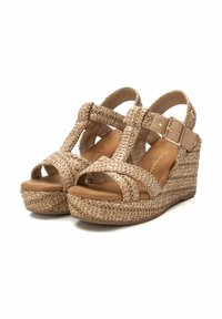 Sandalias de cuña con parte superior de tejido beige, punta abierta, correas entrecruzadas y una hebilla metálica dorada. Cuenta con una suela de plataforma texturizada.