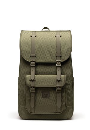 Sac à dos vert olive à motif losange avec sangles à boucle, poche avant et poignée supérieure, debout sur fond blanc.