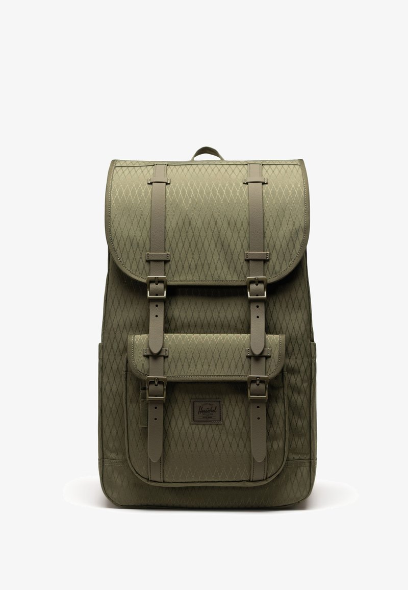 Sac à dos vert olive à motif losange avec sangles à boucle, poche avant et poignée supérieure, debout sur fond blanc.