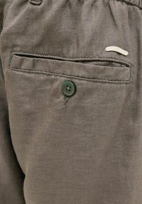 Sötétszürke vászonnadrág egyetlen hátsó zsebbel és zöld gombos záródással. Kis díszítő címke a zseb közelében. Puha tapintású.