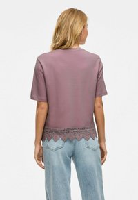 Top de manga corta morado con un dobladillo de encaje texturizado, combinado con unos jeans de pierna ancha en azul claro. Estilo de ajuste relajado.
