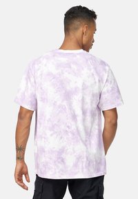 Fialové tričko s vzorem tie-dye, volnějšího střihu, krátkými rukávy a kulatým výstřihem. Disponuje měkkou bavlněnou texturou a bílou základní barvou.