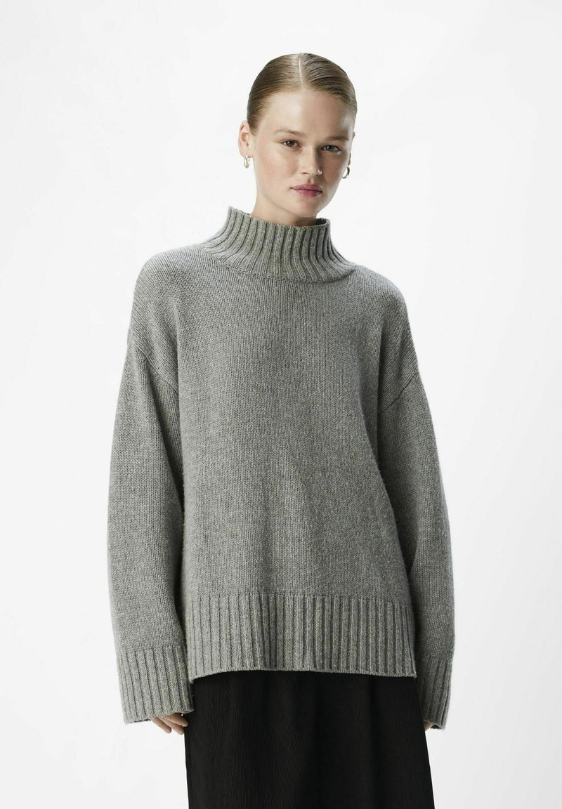 Pull en grosse maille gris avec col roulé et texture côtelée. Le design en tricot présente des manches longues et une coupe décontractée.