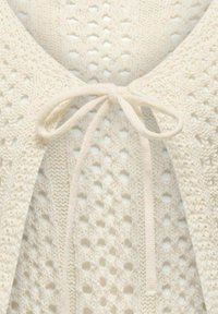 Svetlo krémový pletený kardigán s otvoreným vzorom, zviazaný na krku zodpovedajúcou šnúrkou. Ozdobený jemnými vzormi.