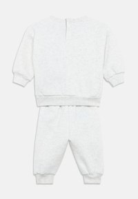 Šviesiai pilkos spalvos džemperio ir kelnių komplektas, pagamintas iš minkštos medžiagos. Viršutinėje dalyje yra ruožuotos rankogaliai ir liemens juosta, taip pat atvartas kaklo nugarėlėje.