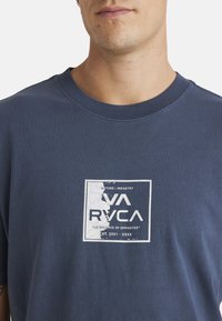 Navy blue cotton t-shirt with a round neck, featuring a white graphic logo print centered on the chest and a slight faded texture.