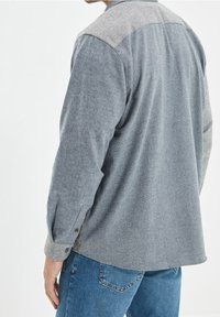 Grau-weiß gestreiftes Hemd mit langen Ärmeln, einer geknöpften Manschette und einem Rückenteil mit Einsatz. Kombiniert mit blauen Jeans.