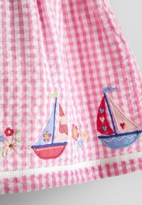 Tessuto vichy rosa e bianco con vele ricamate e fiori colorati lungo il bordo inferiore.