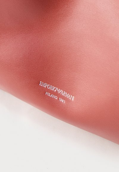 Surface lisse en cuir rose avec logo Emporio Armani embossé en blanc et texte "Milano 1981" en bas.