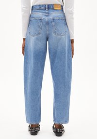 Jeans taille haute bleu clair avec une texture délavée, dotés de cinq poches et d'une étiquette en cuir à l'arrière. Portés avec des talons noirs à clous.