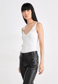 White ribbed tank top with a v-neck design, paired with high-waisted black leather pants featuring side zip detailing.