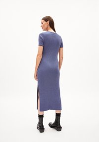 Knielanges, geripptes Strickkleid in Blau mit kurzen Ärmeln und seitlichen Schlitzen. Kombiniert mit schwarzen Stiefeletten. Glatte, dehnbare Textur.