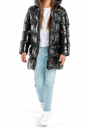 Kind draagt een glanzende zwarte donsjas, wit T-shirt, lichtblauwe spijkerbroek en witte sneakers, loopt naar voren op een witte achtergrond.