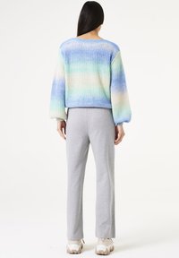 Mehrfarbiger Strickpullover mit einem Farbverlauf in Blau-, Grün- und Cremetönen, kombiniert mit grauen, geraden Hosen und klobigen Sneakers.