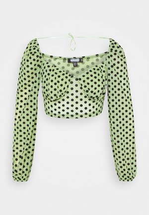 Crop top verde a pois con maniche lunghe a sbuffo, caratterizzato da scollatura quadrata e dettaglio con fiocco sul retro. Realizzato in tessuto trasparente.