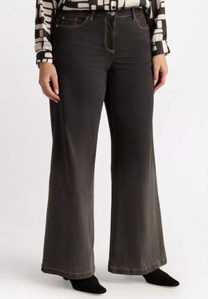 Jeans neri a gamba larga con finitura liscia, caratterizzati da impunture a contrasto e dal classico design a cinque tasche, indossati con una blusa a fantasia.