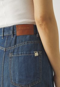 Jeans in denim con un lavaggio blu scuro. Include un'etichetta in pelle marrone con la scritta "WEEKEND MaxMara" e un piccolo tag in tessuto sulla tasca posteriore.