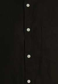 Camicia in lino nera con chiusura frontale a bottoni bianchi, tasca sul petto e finitura in tessuto testurizzato.