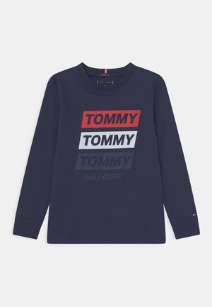 Granatowa koszula z długim rękawem z nadrukiem "TOMMY" powtórzonym trzy razy w kolorach czerwonym, białym i ciemnoniebieskim oraz mniejszym napisem "HILFIGER" w ciemnym kolorze poniżej.