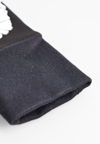 Tela de algodón negra con una textura suave, que presenta un puño acanalado. El diseño incluye elementos gráficos blancos cerca del borde.