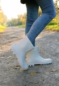 Bottes blanches imperméables jusqu'à la cheville en caoutchouc texturé, avec bout arrondi et semelle antidérapante, portées avec un jean en denim bleu.
