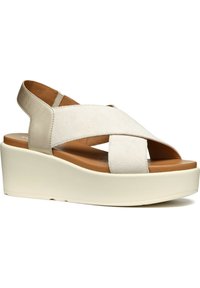 Sandali con zeppa in suede bianco e dettagli beige. Presentano cinturini incrociati e una suola a zeppa di un beige chiaro in contrasto.