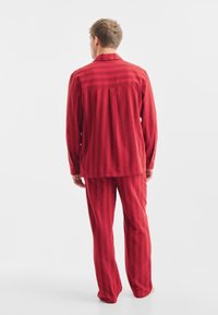 Conjunto de pijama a rayas rojas hecho de un material suave. La camiseta de manga larga presenta puños abotonados, y los pantalones tienen un corte relajado.